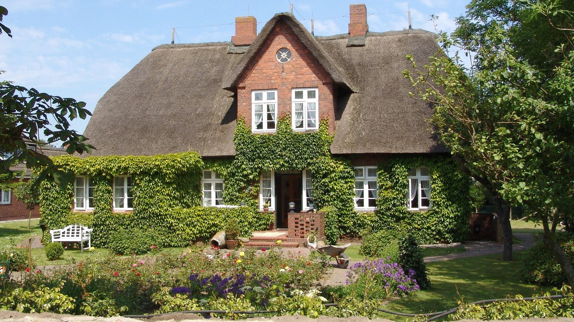 Großes altes Landhaus mit Reetdach, roter Klinkerfassade und grünem Garten – Symbolbild für eine Immobilie, die man vererben kann.