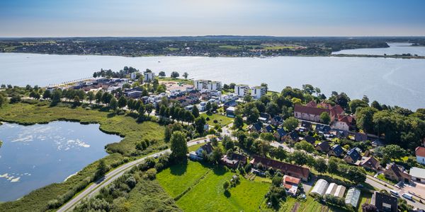Luftbild der Stadt Schleswig mit Flussufer, Wohnsiedlungen, Einzelhäusern, Feldern und Waldflächen bei klarem Himmel